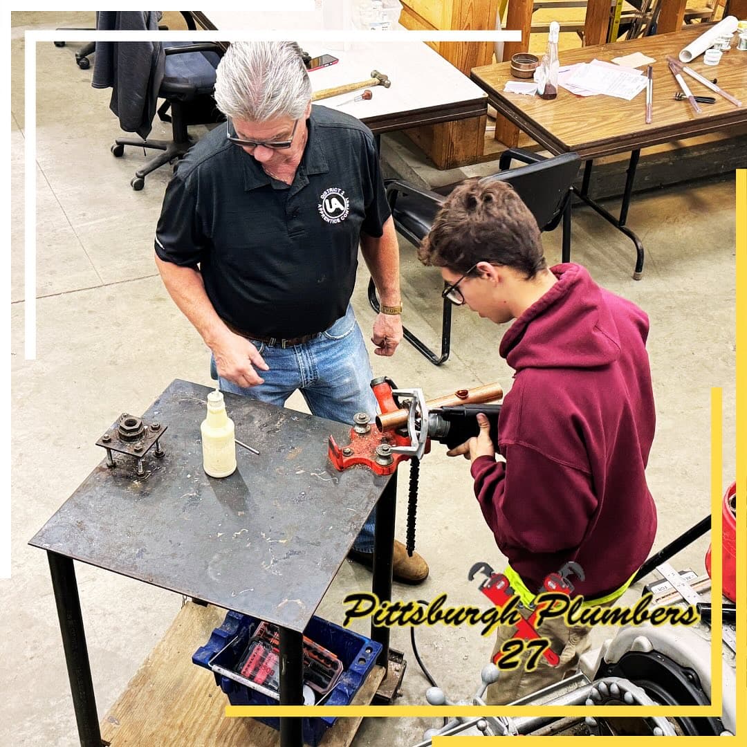 A veteran UA Local 27 journeyman teaching a young apprentice — the kind of plumber dispatched on a leak detection call.
